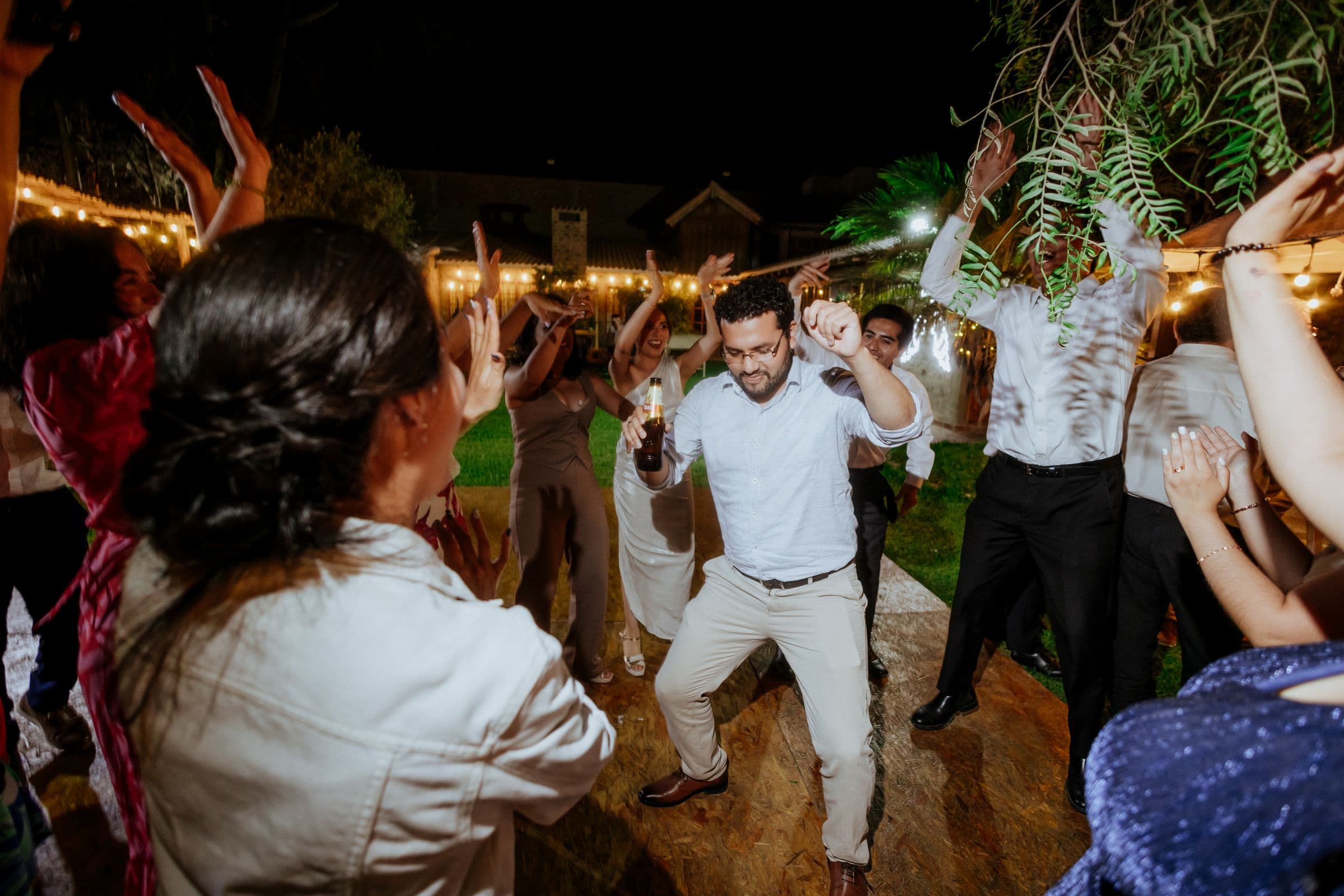 Guests in a dance circle clapping under string lights at night