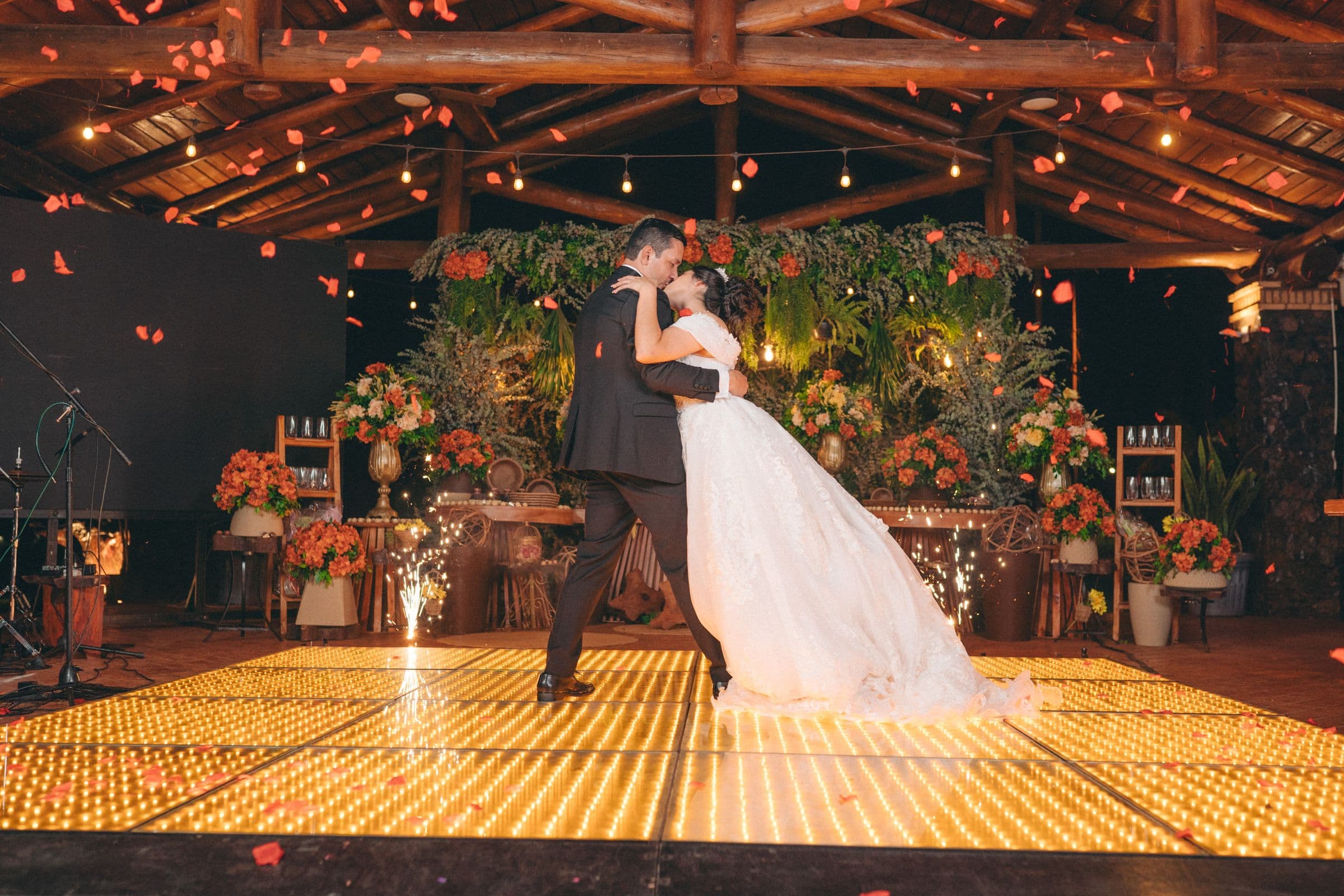 A couple dancing on a lit dance floor as petals fall around them